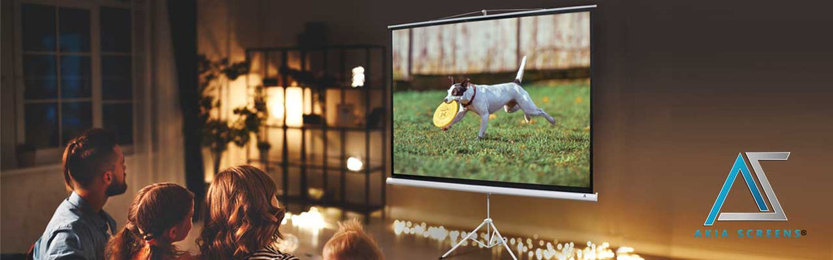 A large projection screen on a tripod displays a dog playing with a frisbee in a backyard, while several people sit in a dimly lit living room watching. A logo for 'Area Screens' is visible in the bottom right corner.